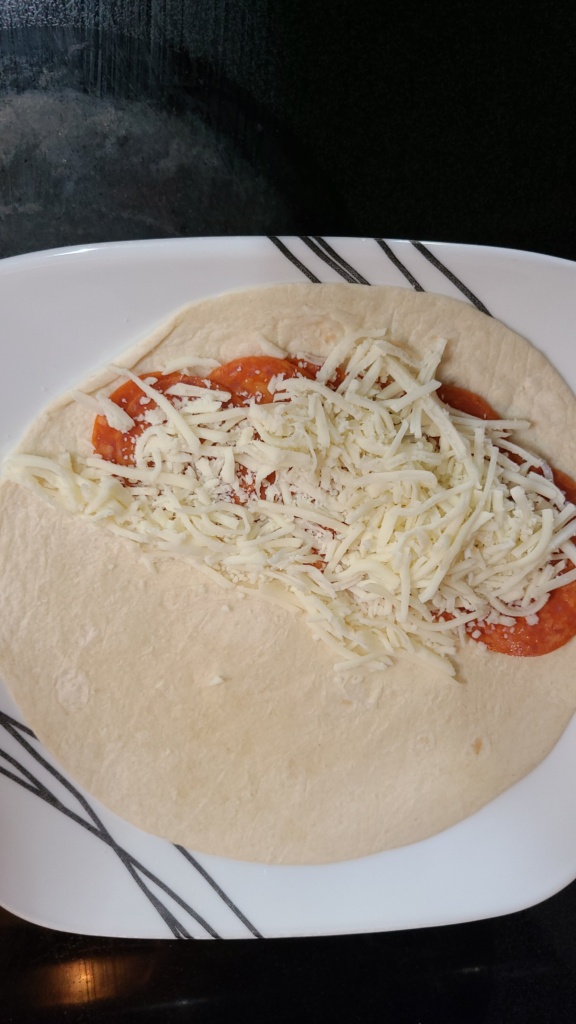 A tortilla with pepperoni and shredded mozzarella on top