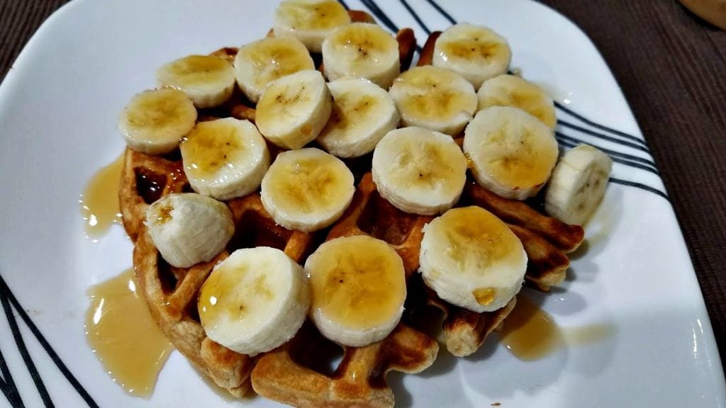 An image of a waffle on a plate topped with a sliced banana and syrup