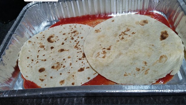 Image of a 9x13 pan with tomato sauce and tortillas