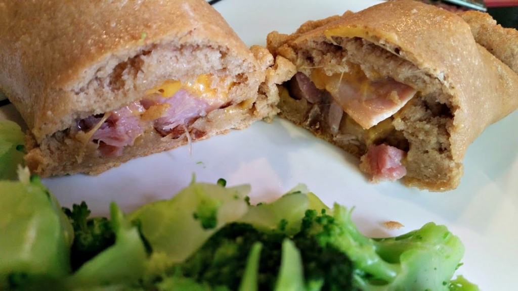 A homemade ham and cheese calzone on a plate with a side of broccoli