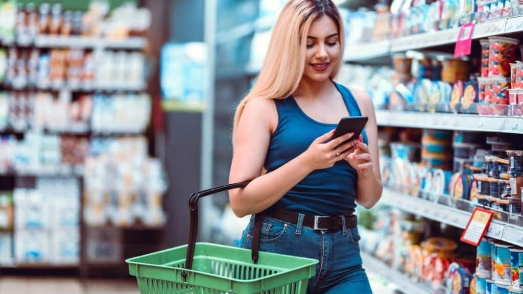 A woman holding a shopping basket, looking at her phone