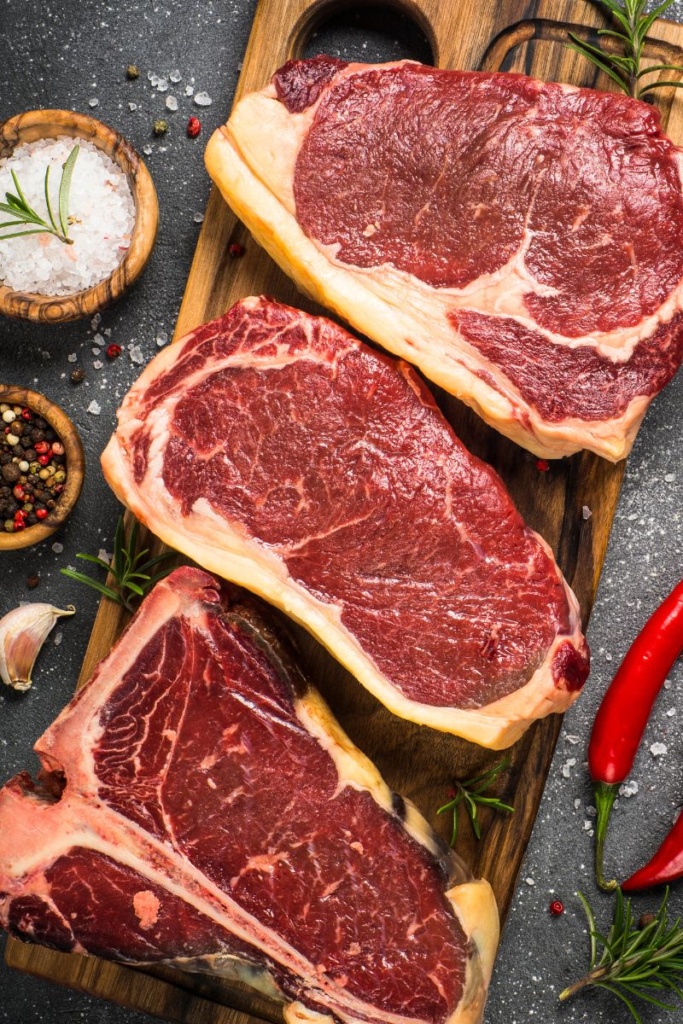 3 large steaks on a wooden cutting board