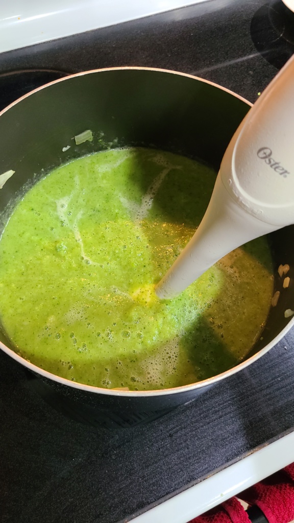 A large pot of broccoli cheese soup, blended with an immersion blender