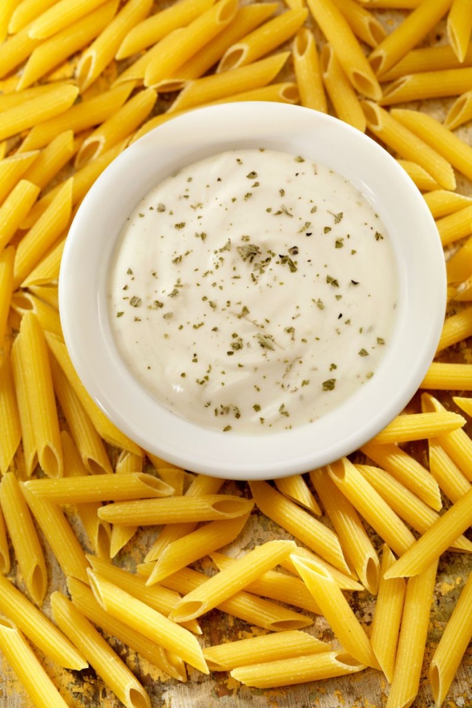 A bowl of Alfredo sauce surrounded by dry pasta