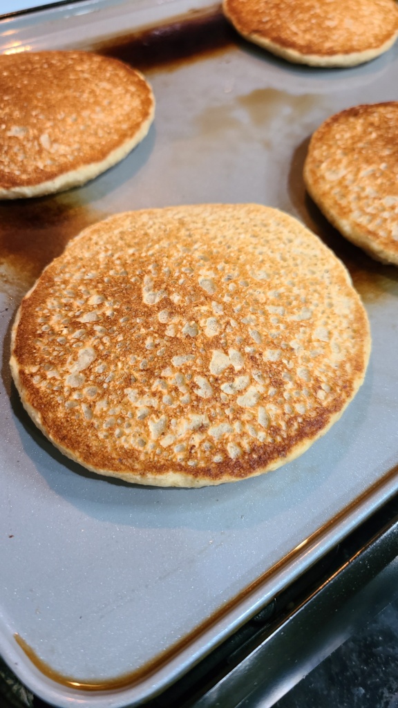 Pancakes cooking on a griddle, with a golden brown top