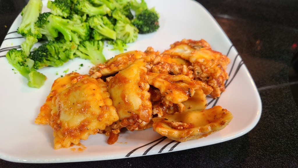 Ravioli in a meat sauce on a plate, with steamed broccoli.