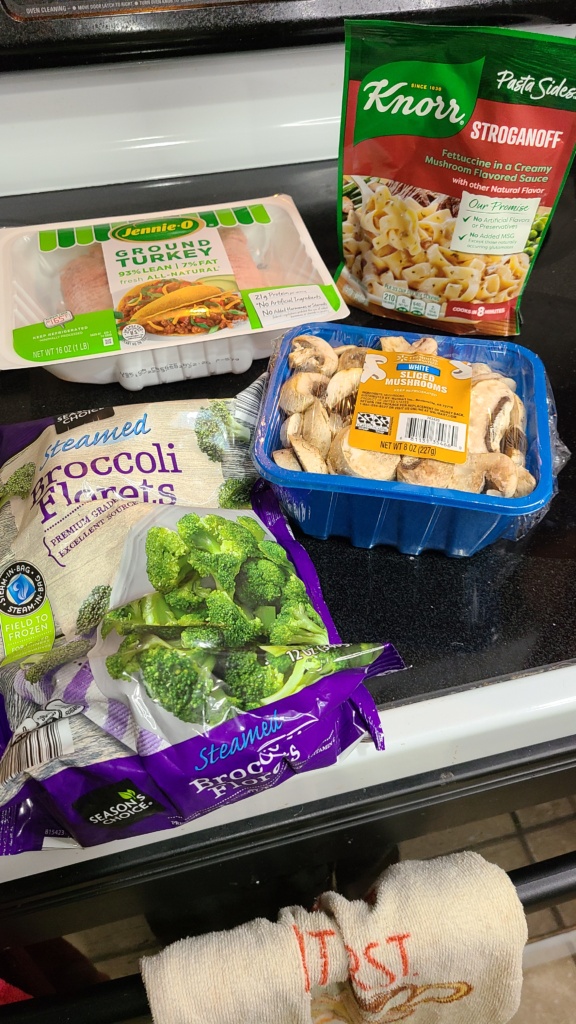 A packet of Knorr stroganoff, a package of ground turkey, white mushrooms, and a bag of frozen broccoli