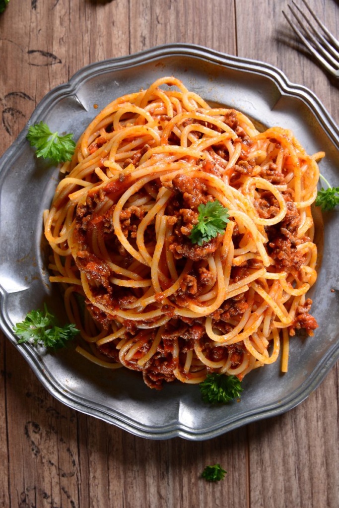 A bowl of spaghetti and meat sauce on a blue plate