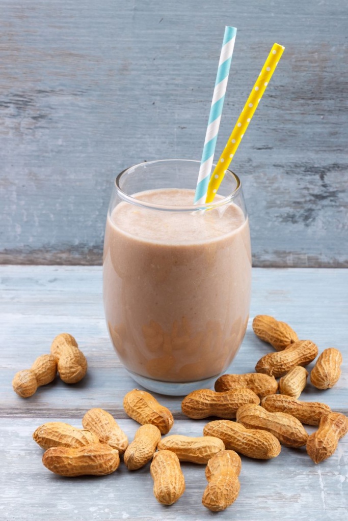 A glass filled with a smoothie, surrounded by peanuts