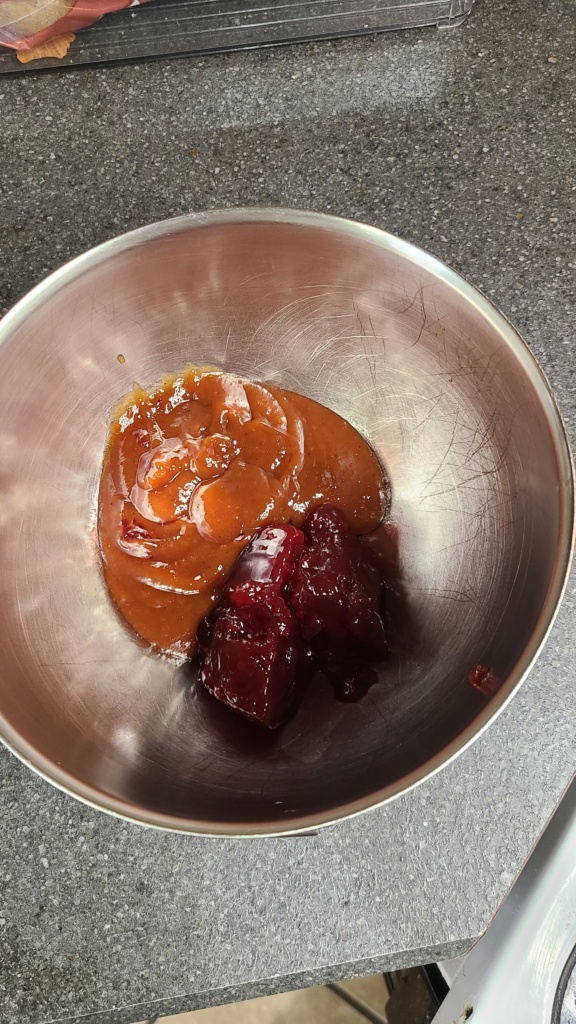 A metal bowl with BBQ sauce and cranberry sauce inside