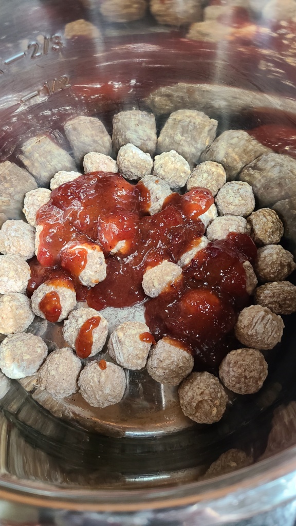 A slow cooker with frozen meatballs and a cranberry sauce mixture