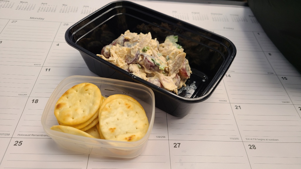 A meal prep container with chicken salad, next to a small container with pita crackers