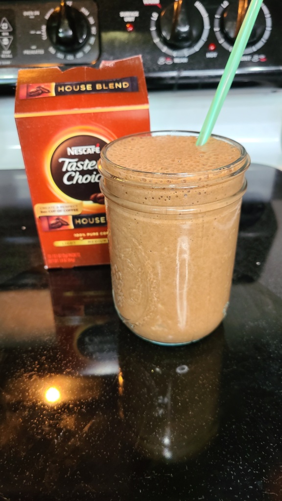 A Mason jar filled with chocolate coffee smoothie. Behind it is a box of instant coffee packets.