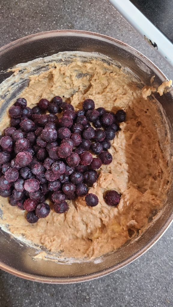 A bowl full of muffin mix, topped with frozen blueberries