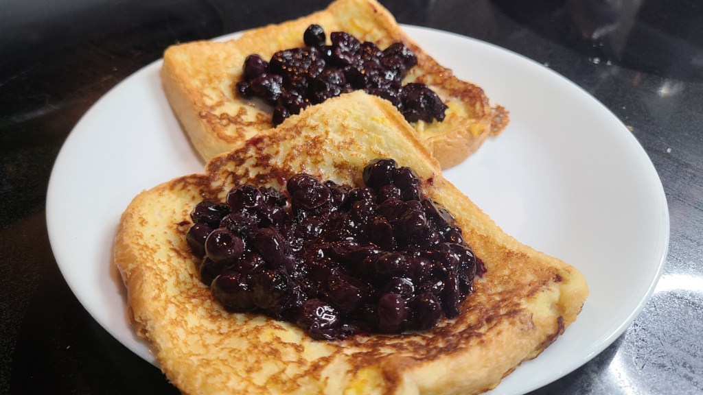 Two pieces of French toast on a plate, topped with blueberry sauce