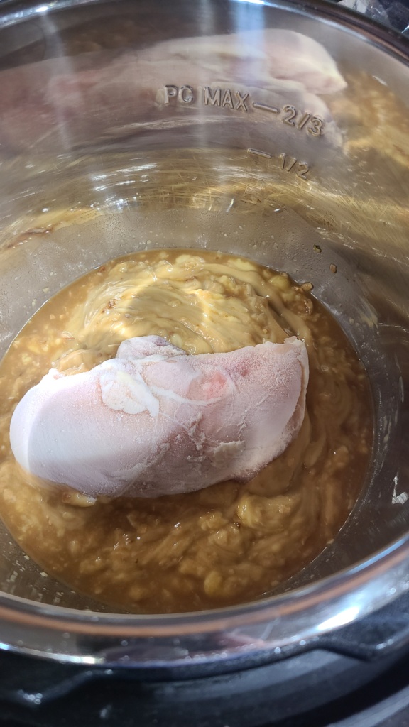 A slow cooker filled with uncooked ingredients for French onion chicken