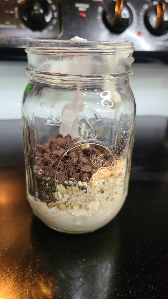 A Mason jar filled with unmixed ingredients for chocolate chip overnight oats