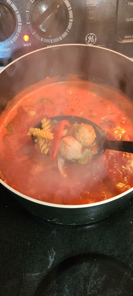 A large pot filled with boiling meatball soup and uncooked pasta
