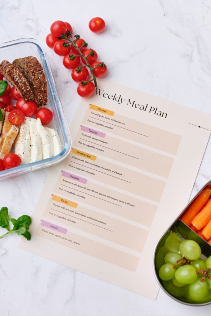 A piece of paper that says "Weekly meal plan". Next to it is a meal prep container filled with chicken and vegetables.