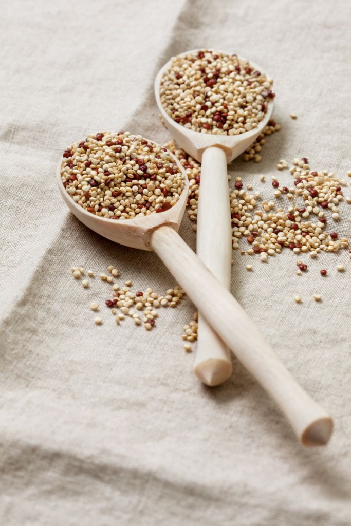 Two wooden spoons on a white cloth, filled with dried quinoa