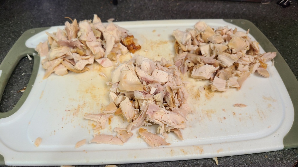 Shredded chicken on a cutting board, divided into 3 portions