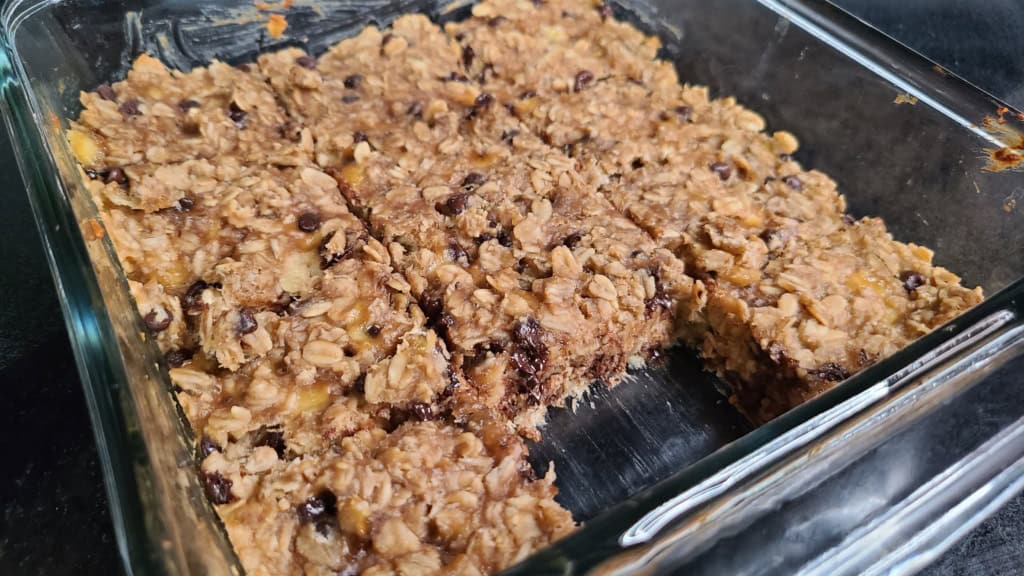 A baking dish with baked banana oatmeal bars. They are cut and one is missing from the dish.