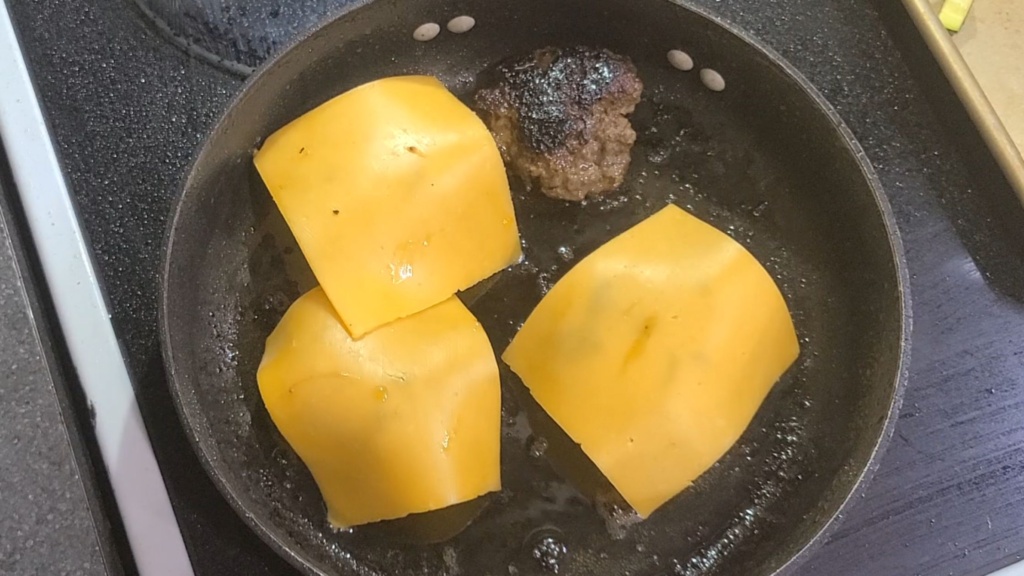 Cooked burger patties topped with sliced cheddar cheese