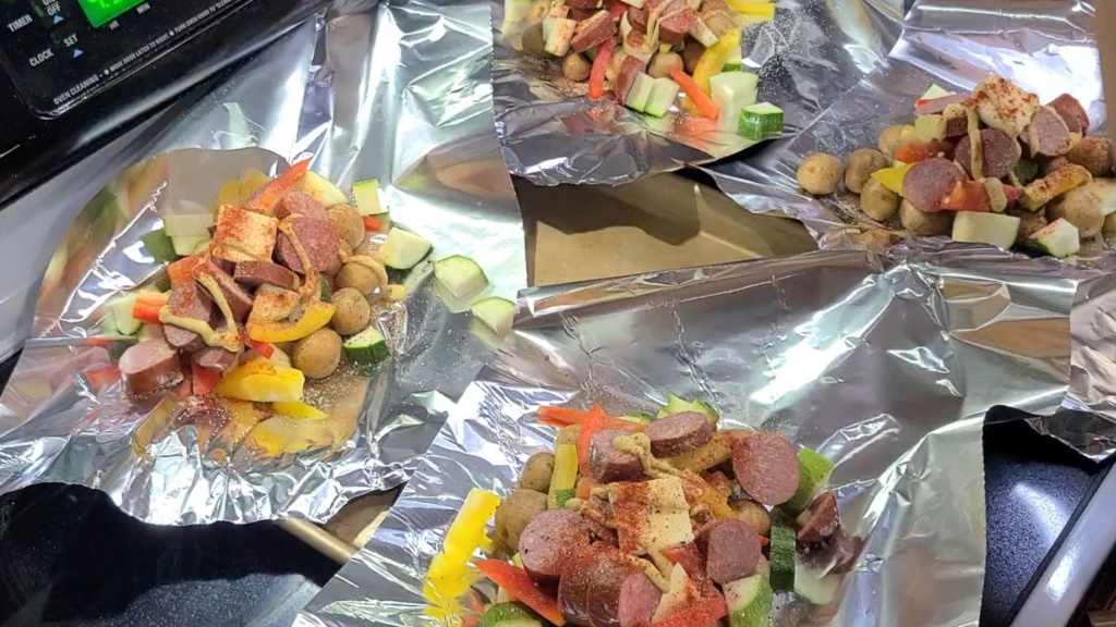 Two sheet pans with kielbasa ingredients sitting on aluminum foil