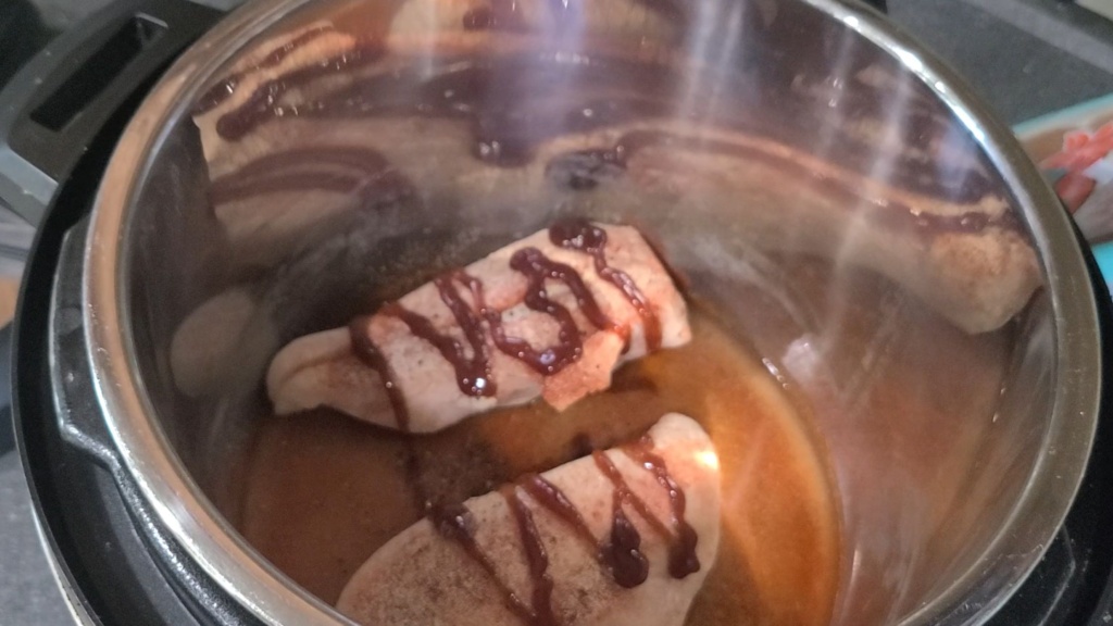 2 chicken breasts in a slow cooker, drizzled with BBQ sauce.