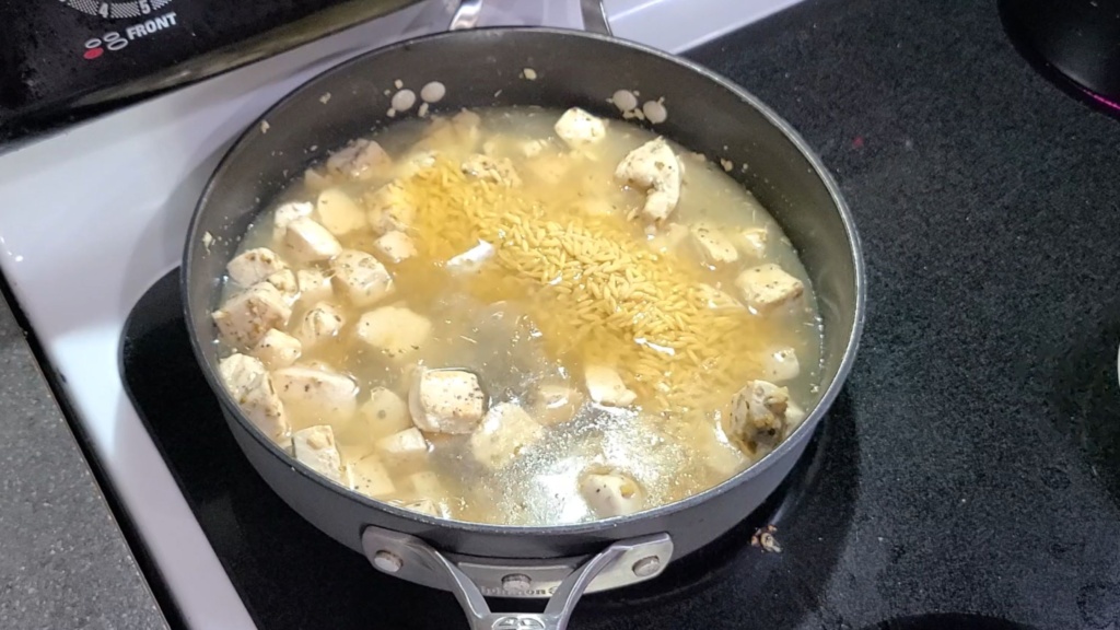 A skillet with cubed chicken, broth, and orzo