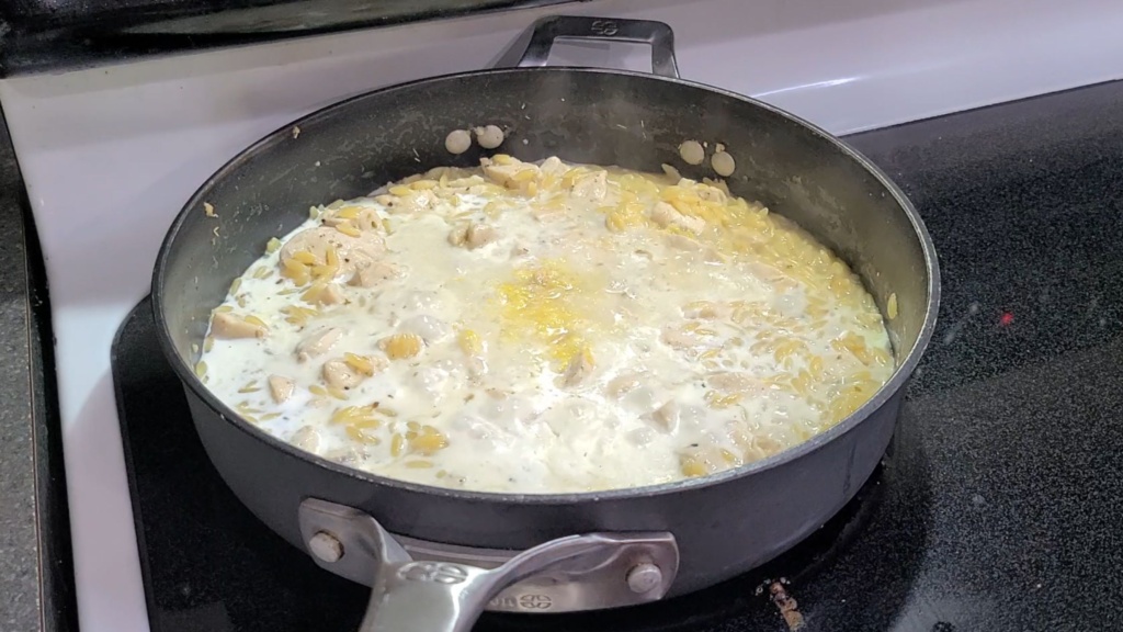 Chciken and orzo cooking in a skillet filled with broth