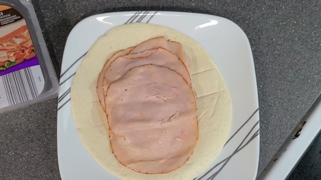 A tortilla on a plate, with deli turkey on top